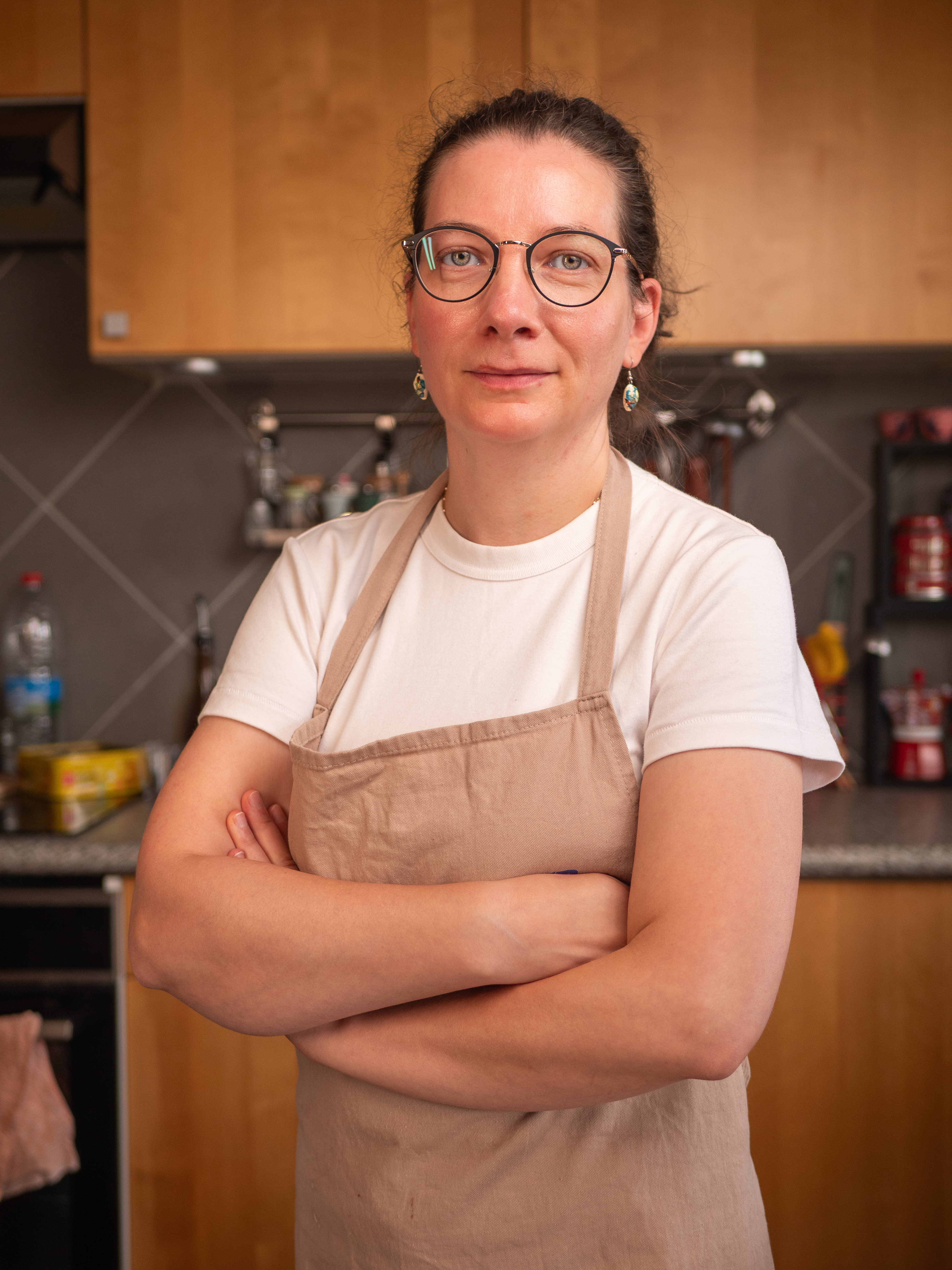 Portrait d'Aurore Borégale, bras croisés dans sa cuisine, en tablier