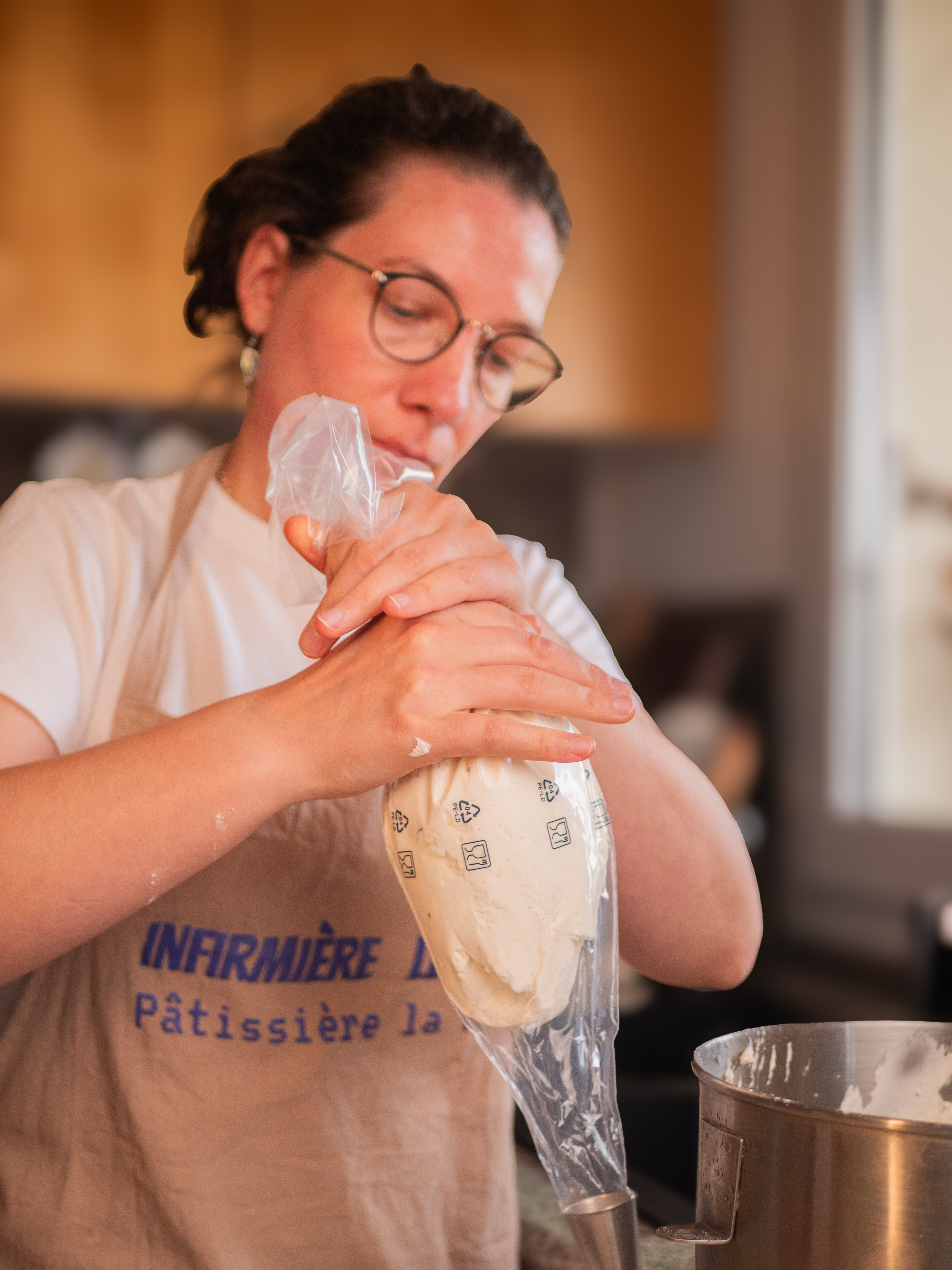 Aurore remplit une poche à douille de crème, en tablier « Infirmière le jour, pâtissière la nuit »