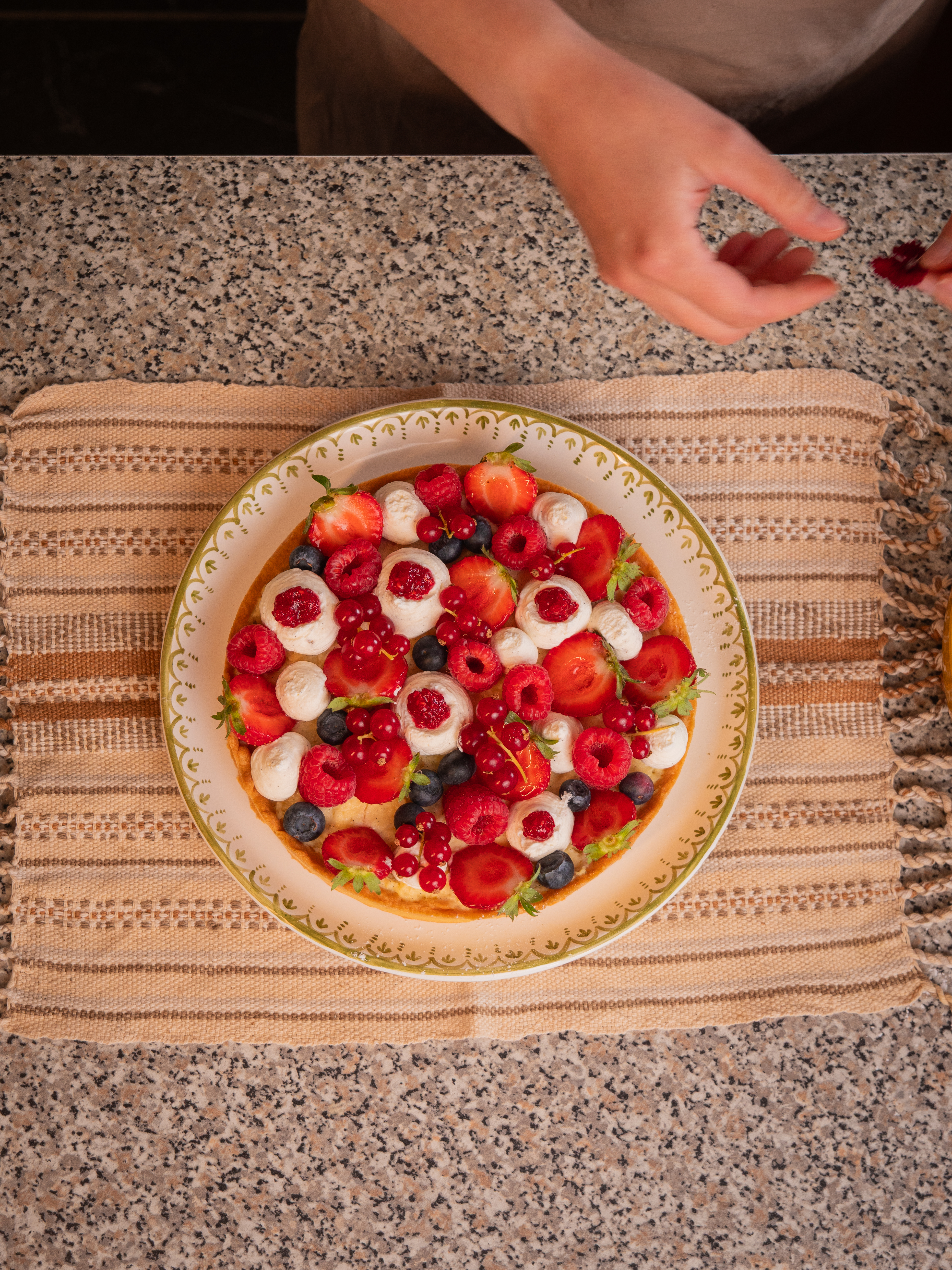 Tarte aux fruits rouges vue du dessus, une main dépose une dernière groseille