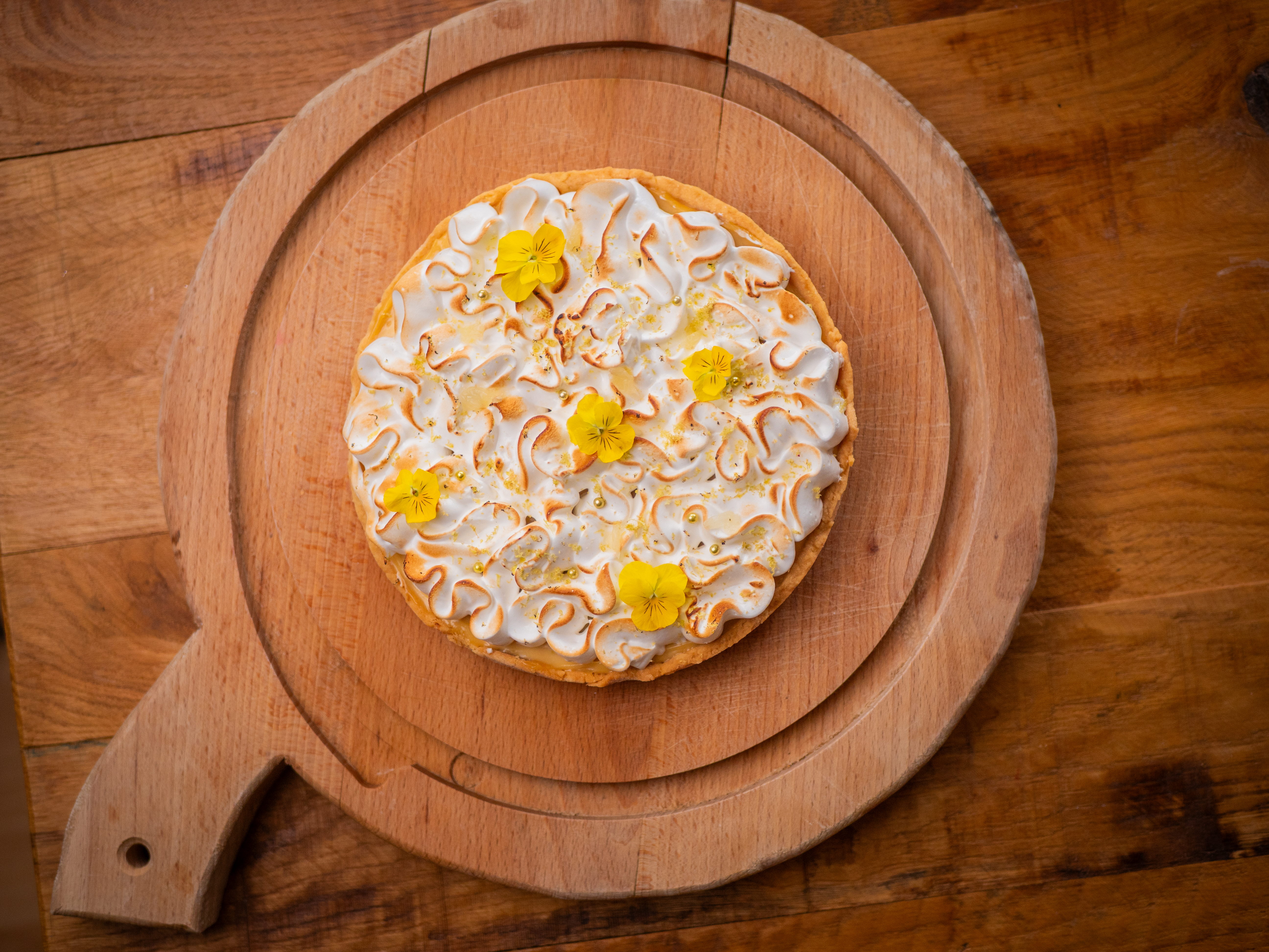 Tarte au citron meringuée vue du dessus, décorée de fleurs comestibles, sur une planche en bois