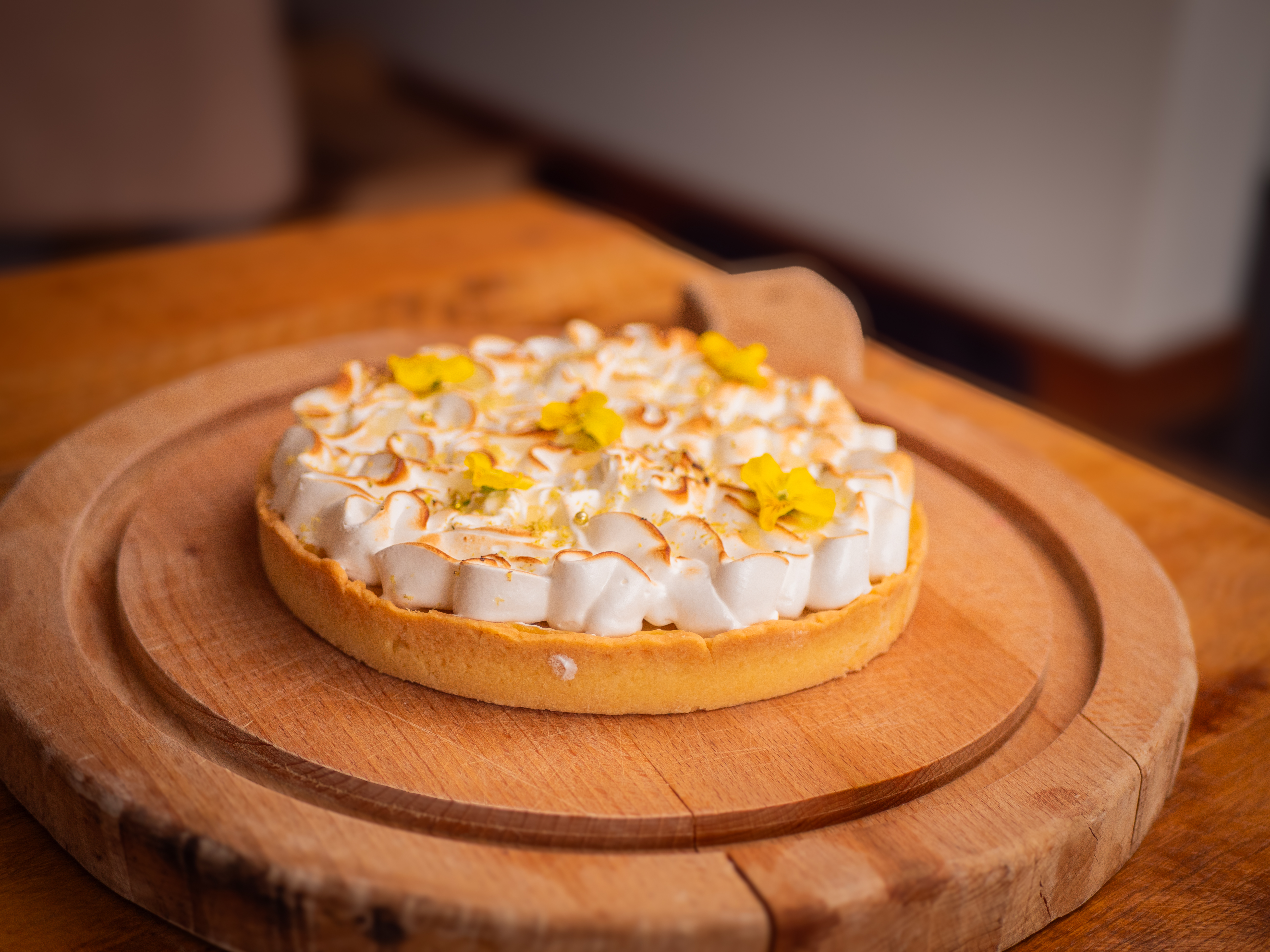 Tarte au citron meringuée décorée de fleurs comestibles, sur une planche en bois