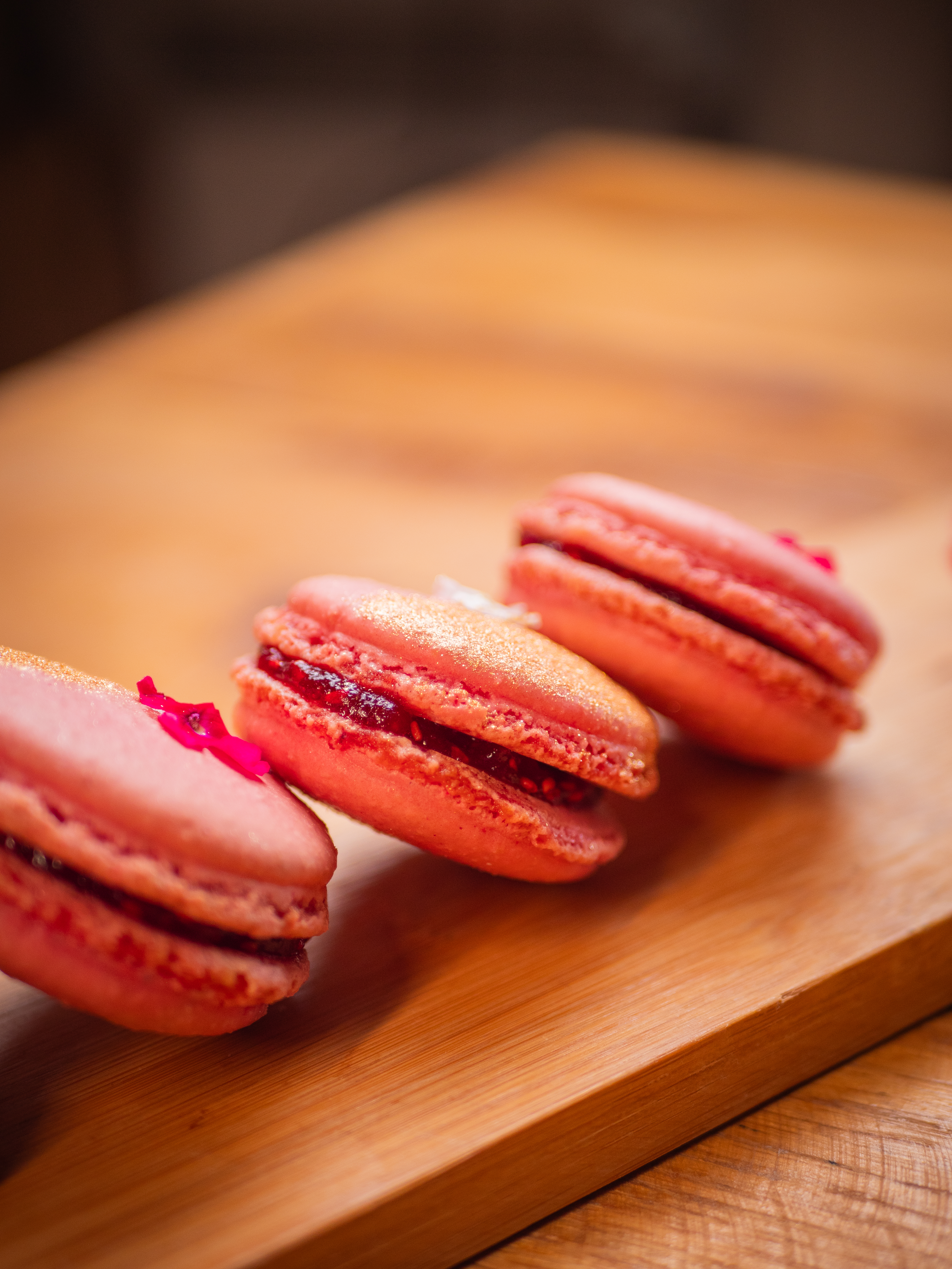Macarons roses pailletés d'or, à la garniture rouge, sur une planche en bois